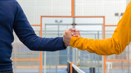 Male padel players handshake after win a padel match in a blue paddel court indoor. Tennis players...