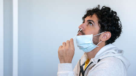 Portrait of relaxed man wearing mask and taking a self swabbing home tests for with antigen kit....