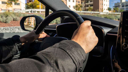 Cropped of man driving car, over shoulder shot. Unrecognizable caucasian driver holding hands on steering wheel, driving brand new nice automobileの写真素材