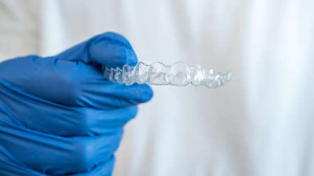 Male hand in gloves holding dental aligner retainer on white background of dental clinic for...
