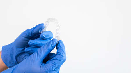 Adult man with gloves holds invisalign transparent braces for dental correction. Caucasian person holding invisible orthodontic retainer and aligner with white copy space.の写真素材