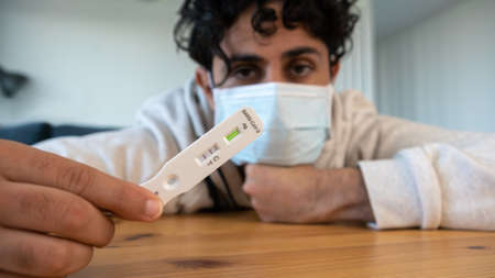 Face of unhappy adult man holding a positive test device for Covid19. Sad caucasian person showing...