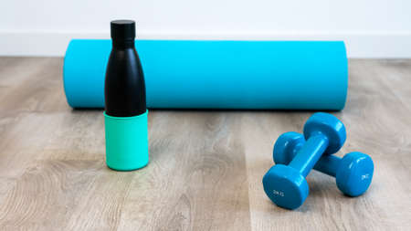 Exercise with two blue dumbbells with modern eco water bottle and mat preparing for yoga sports...