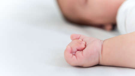 Hand of little baby on white sheet bed background with day light. Cute boy and chubby hands of a...