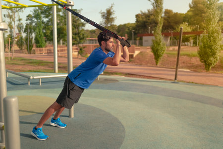 Sportsman working out with system outside. Total body resistance exercises in city park. A handsome...