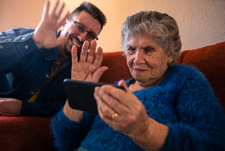Grandmother talk on webcam phone call with her grandson. Grandma in blue sweater sit on sofa for...