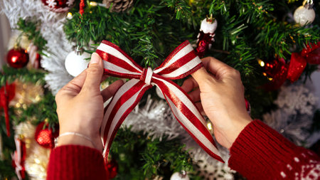 Woman decorating christmas tree with beautiful red and white bow. Girl decorated with holiday ribbon Xmas ornaments. New year decoration design elementの写真素材