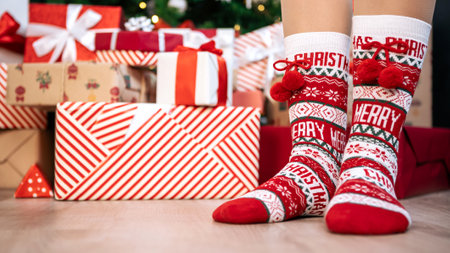 A young girl with warm socks and copy space. Woman enjoys the winter season in the comfort of her home and a box of surprise gifts by Christmas tree, creating a happy and cozy holiday celebrationの写真素材