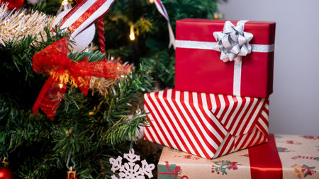 red Neatly wrapped gift boxes beneath the contemporary Christmas tree in a home, complemented by holiday Xmas ornaments, a festive for New Year decor.の写真素材