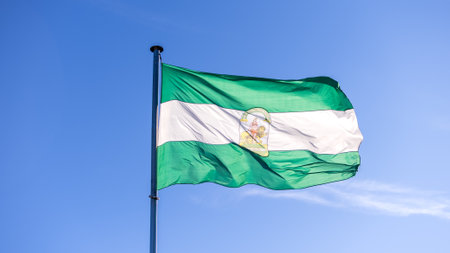 The current flag of Andalusia waving in wind with blue sky. Andalusian banner blowing, soft and smooth silk. Cloth fabric texture ensign background. Wear it for national day. Spanish federal stateの写真素材