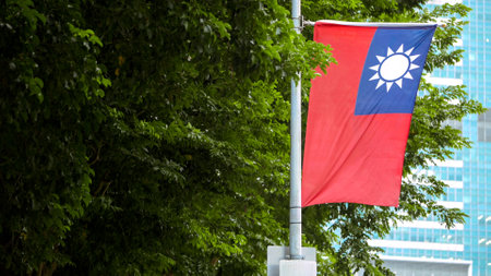Taiwan's flag waving on a pole surrounded by lush green leaves, symbolizing national pride amidst nature.の写真素材
