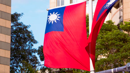 A pair of Taiwan flags waving gracefully on a pole, set against a backdrop of trees and a modern building, symbolizing Taiwanese pride and heritage.の写真素材