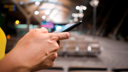 A closeup of hands using a smartphone in an airport terminal. Modern seating and curved architecture, technology and travel. Woman typing a quick message on a phone at airportの写真素材