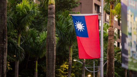 Taiwan's flag waving on a pole surrounded by lush green leaves, symbolizing national pride amidst nature.の写真素材