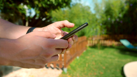 Person holding a smartphone in backyard. Man hands holding a phone in garden.