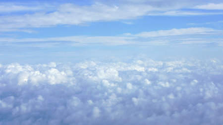 Scenic aerial view of fluffy white clouds with a hint of the Earth horizon captured during a flight. Perfect for nature and travel themes. A serene and expansive elevated perspective.の写真素材