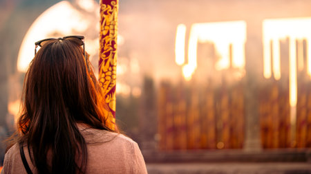Back view of woman admiring giant incense burning at temple in Taichung, Taiwan, surrounded by golden light and sacred atmosphereの写真素材