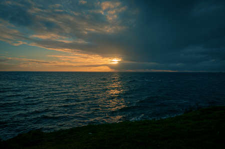 Sunset over the sea with clouds in the sky and green grassの写真素材