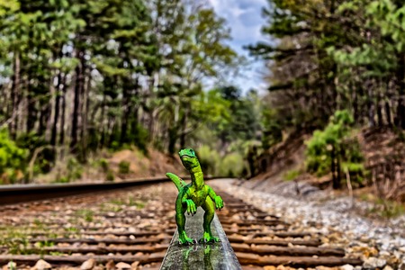 Green Velociraptor dinosaur  walking on  rail railroad tracksの写真素材