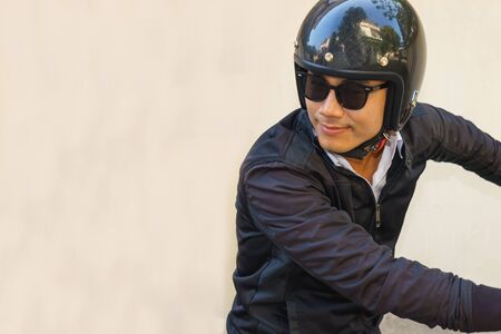 Young Asian motorcyclist wearing black jacket is looking back while riding his motorcycle.の写真素材