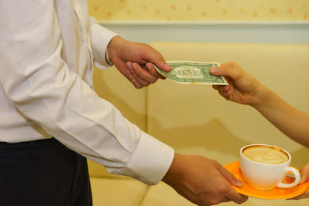 Woman hands one dollar banknote for tip to waiter after received latte.の写真素材