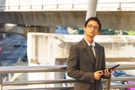 Middle aged Asian businessperson is holding tablet and thinking about his business.の写真素材