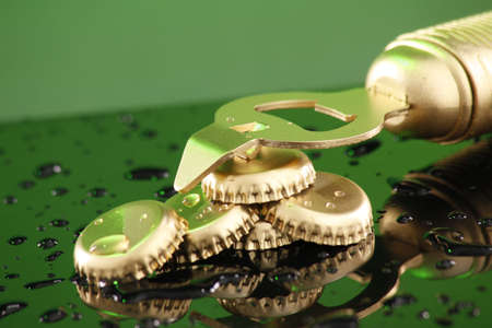 Golden beer caps on a wet countertop under green lightの写真素材