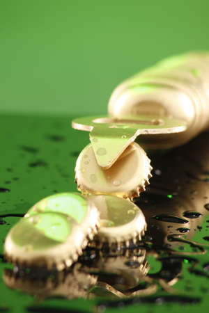 Golden beer caps on a wet countertop under green lightの写真素材