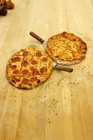 Pre cut plain mozzarella and mozarella with pepperoni pizza on the baker's tableの写真素材