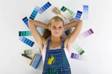 Young smiling blonde wearing dungarees. Lying on floor among color palettes and paintbrush. Looking at cameraの写真素材