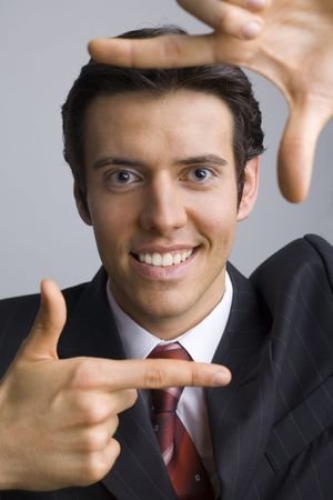 Smiling, handsome businessman. Showing his face by hands. Looking at camera. Gray background, frontの写真素材