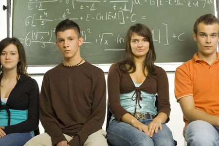 Small group of teenagers sitting in front of blackboard. Two boys and two girls. Looking at camera,...