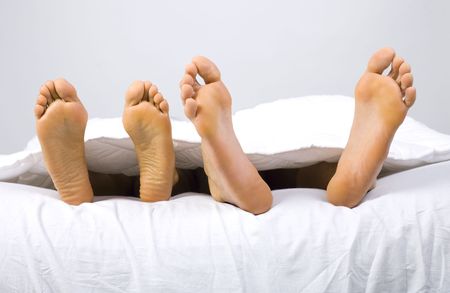 Foots of young couple lying in bed. Gray background, front view の写真素材