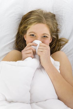 Young smiling woman lying in bed. Hiding under duvetの写真素材