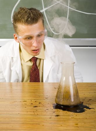 Young dejected chemist sitting in front of smokey beaker with opened mouth. Green backgroundの写真素材