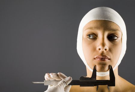 Young, beautiful woman with bandage on head. Somebody in rubber glove holding calliper. Front view,...