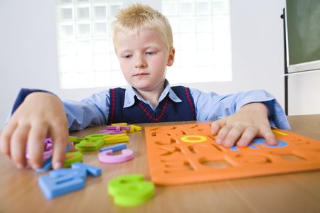 Young boy sitting at desk and making letters jigsaw. Front view.