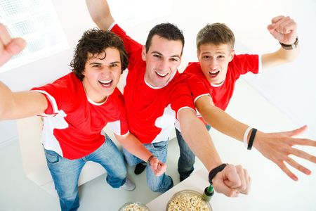 Three happy sport's fans get up from couch with raised hands. They looking at camera. High angle view.の写真素材