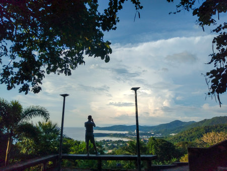 Man sitting on the balcony with a view of the sea and mountainsSilhouette of Man Photographing...