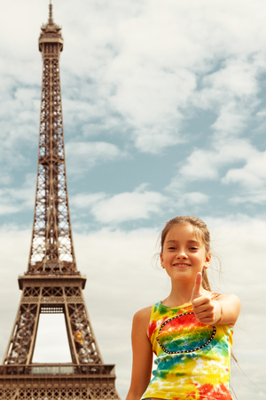Cheerful smiling girl tourist showing thumbs up success sign in front of Eiffel Tower, Paris.の写真素材