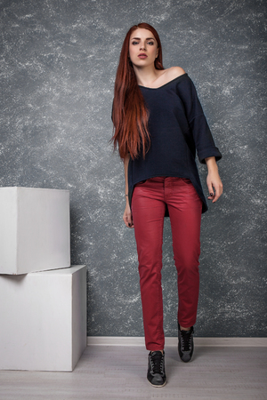 Full Length Portrait of Trendy Hipster Girl Standing at the Gray Wall Background. Urban Fashion Conceptの写真素材