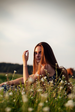 pretty teenager girl with healthy long hair sitting on the meadow in summer day.の写真素材
