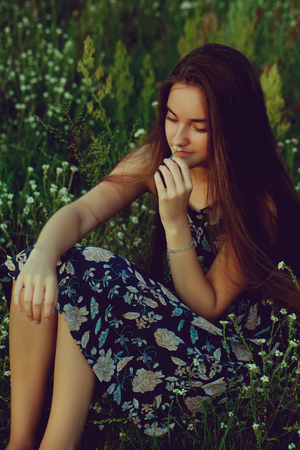 pretty teenager girl with healthy long hair sitting on the meadow in summer day.の写真素材