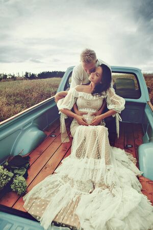Pregnant woman and her husband happy together and looking each other with love. Outdoor photoshoot near the carの写真素材
