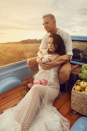 Pregnant woman and her husband happy together and looking each other with love. Outdoor photoshoot in the carの写真素材