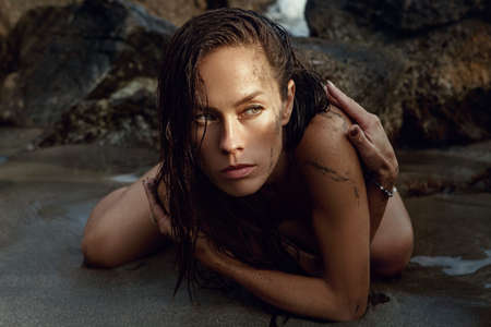 Beautiful woman posing on a beach. Wet hair, sand on the skinの写真素材