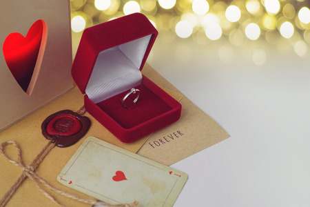 Engagement ring in a red velvet box. Envelope with wax seal and heart playing card. Space for textの写真素材