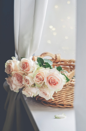 Bouquet of pale pink cream roses in a woven basket on a windowsill. Soft focus. Romance background with copy space.の写真素材