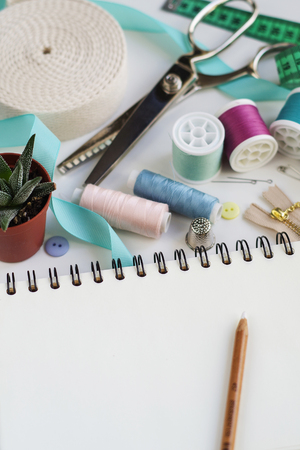 Blank notepad with pencil surrounded with spools of thread and basic sewing tools including pins, needle, a thimble, and tape measure. Copy spaceの写真素材