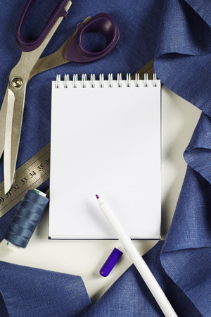 Top view tailor accessories and tools. Blank notepad surrounded with cutting scissors, spools of thread, violet fabric. Copy space for your textの写真素材